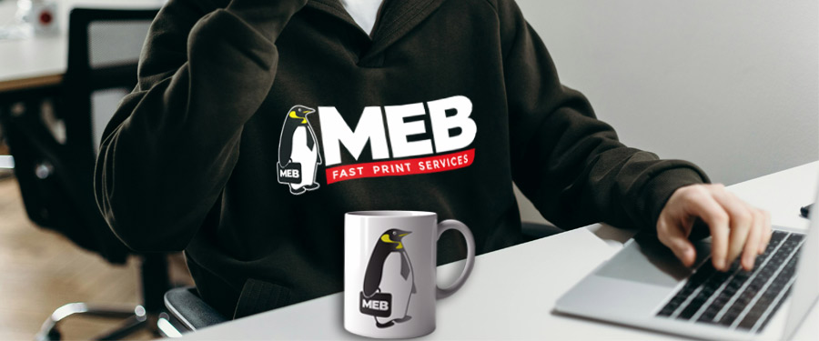 Toimistotyöntekijä, jolla on yllään MEB:n painattama brändihuppari ja pöydältä löytyy muki MEB:n pingviinimaskotin painatuksella