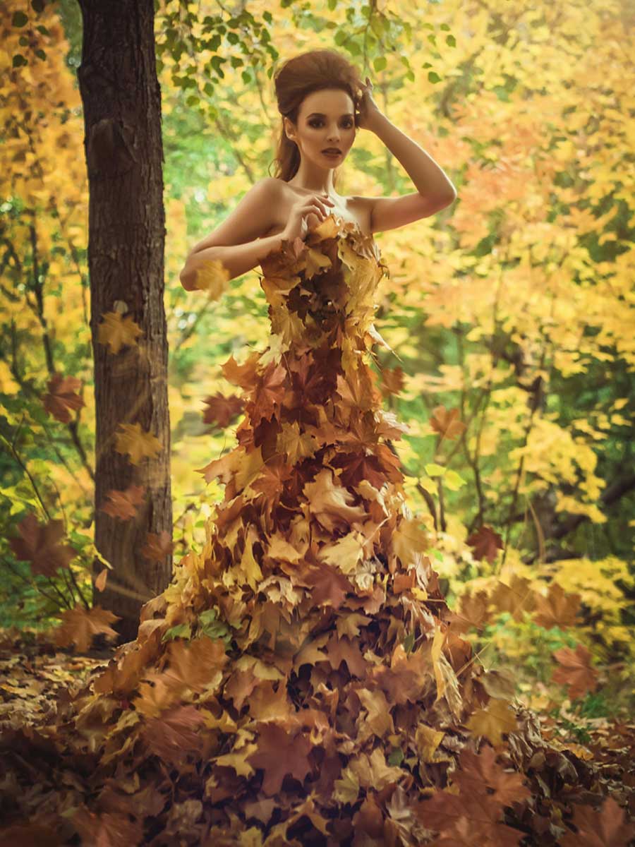 A top model in an Autumn forest with dress covered in yellow and orange leaves